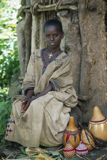 ETHIOPIA, Harerge Province, General, Young girl sitting in front of tree trunk with decorated gourds at her feet.