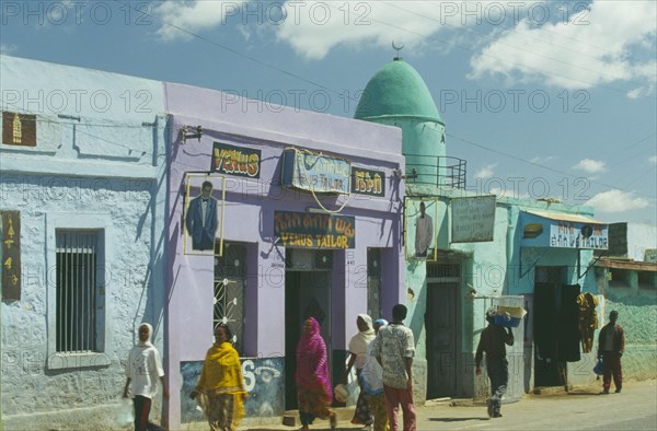 ETHIOPIA, Harerge Province, Harer, Mosque painted turquoise with domed roof situated between two tailors.  People walking past.