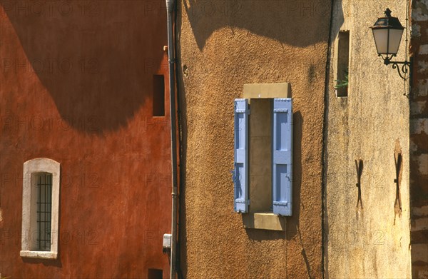 FRANCE, Provence-Cote d’Azur, Vaucluse, Roussillon.  Architectural detail of ochre and terracotta coloured walls with blue window shutter and wall lamp.