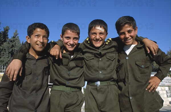 SYRIA, Central, Hama, "Four smiling schoolboys in uniform, standing in a line with their arms around each others shoulders.  Three quarter view. "