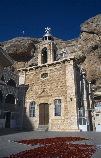 SYRIA, South, Maaloula, "Deir Martalka, the Convent of St Takla.  Exterior and bell tower with flower petals laid out on rugs in the courtyard and steep, eroded cliff face behind."