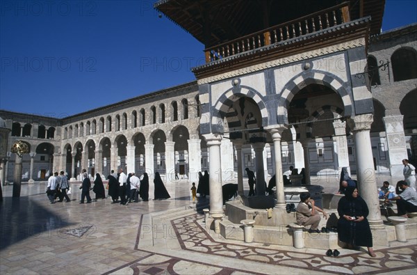 SYRIA, South, Damascus, The Umayyad Mosque.  The ablutions fountain with pilgrims sitting around the hexagonal base and crossing the marble courtyard floor at its left.