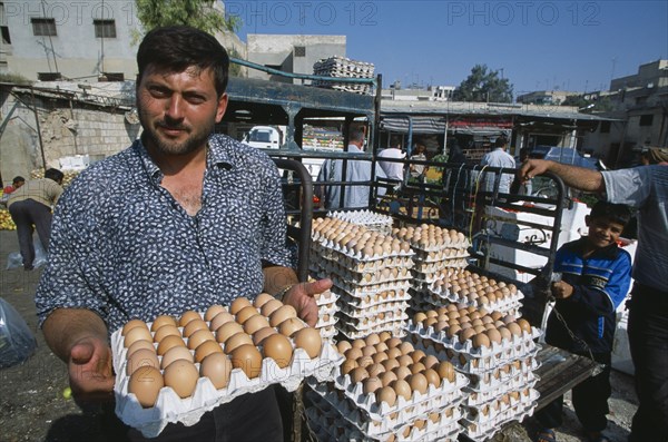 SYRIA, Central, Hama, "Man selling eggs in street market, standing holding tray with more stacked behind him. "