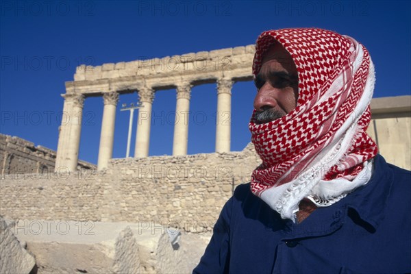 SYRIA, Central, Tadmur, "Custodian to the Sanctuary of Bel in traditional red and white checked head-scarf,gutra or kiffeiya.  Ruins of colonnaded portico behind. "