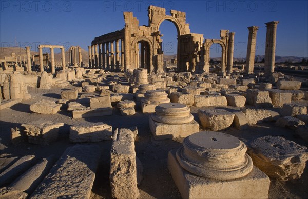 SYRIA, Central, Tadmur, Monumental arch.  High central arch flanked by a lower arch on each side with colonnaded street part seen  behind and masonry ruins in the foreground. Palmyra