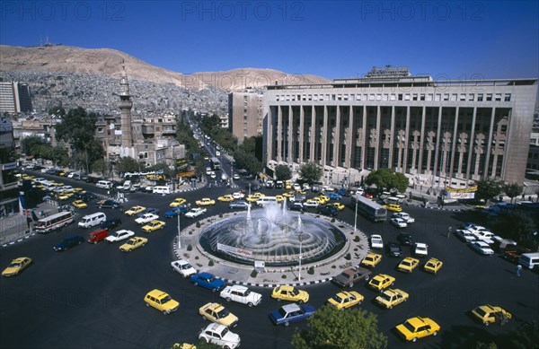 SYRIA, South, Damascus, View over Tajrida Al Maghribiya Square with traffic encircling a central fountain. Modern facade of the Central Bank top right.