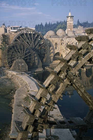 SYRIA, Central, Hama, Wooden norias or waterwheels on the Orontes river and the Al-Nuri Mosque dating from 1172 and built of limestone and basalt.  Large section of a wheel in the immediate foreground.