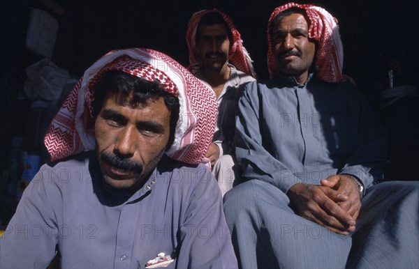 SYRIA, Central, Tadmur, "Two seated men wearing traditional red and white checked headscarves, gutras or kiffeiyas."