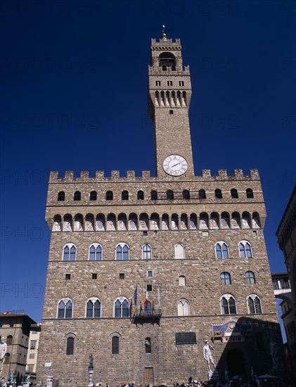 ITALY, Tuscany, Florence, Palazzo Vecchio.  Facade of medieval palace completed in 1322 and used as the town hall.  Crenellated roof and clock tower with statues outside entrance including copy of Michelangelos David.