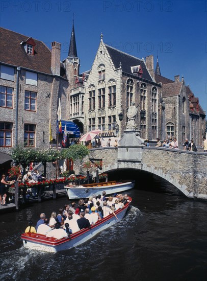 BELGIUM, West Flanders, Bruges, Tourists on canal boat trips below a bridge and old buildings