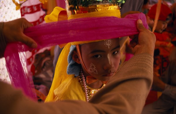 THAILAND, Chiang Mai, Novice monk at ordination ceremony at Wat Chiang Yuen having ornate head dress put on.