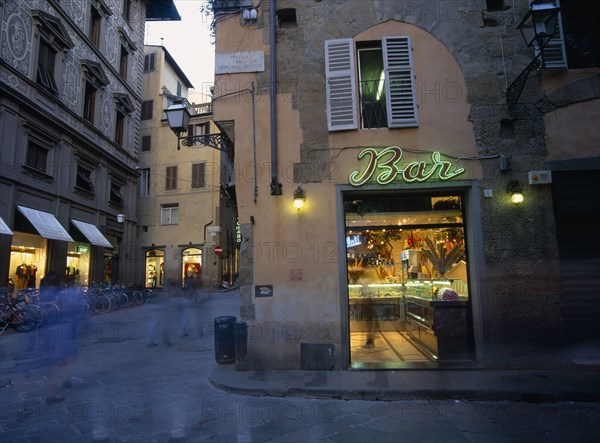 ITALY, Tuscany, Florence, Ice cream bar with neon sign illuminated at night in narrow street with pedestrians in blurred movement.