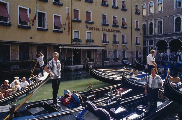 ITALY, Veneto, Venice, "Gondolas tied up at Hotel Cavalletto, with gondolier and tourist passengers partly seen behind.  "