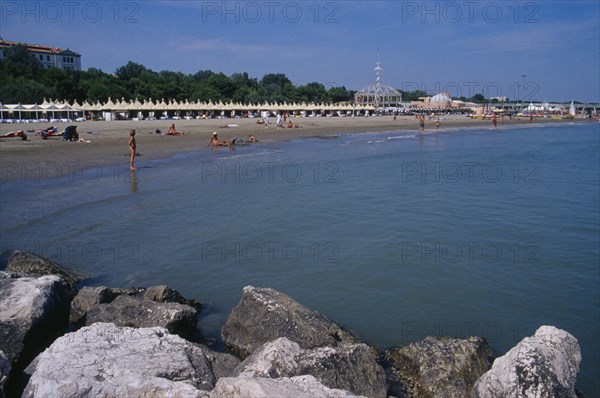 ITALY, Veneto, Venice, "Lido Beach with sun bathers, distant view with rocks in the foreground. "