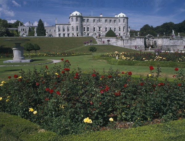 IRELAND, County Wicklow, Powerscourt House, View over formal gardens towards exterior facade.  Flowerbed with red and yellow roses in the immediate foreground.