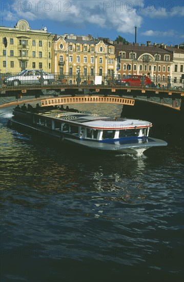 RUSSIA, St Petersburg, Moika Canal with tour boat passing underneath arched bridge with cars crossing and traditional houses behind.