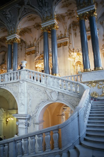 RUSSIA, St. Petersburg, The Winter Palace of the Hermitage Museum.  Detail of the Jordan Staircase and opulent white and gold interior decoration and marble columns.  Visitors on balcony.