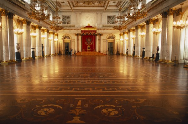 RUSSIA, St. Petersburg, "Winter Palace of the Hermitage, Hall of St. George.  Interior lined with columns and gold candelabra with lights reflected on polished floor surface."