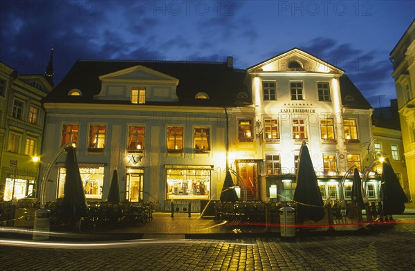 ESTONIA, Tallinn, Raekoja Plats.  Exterior of cafe and restaurant and clothes shop illuminated at night.