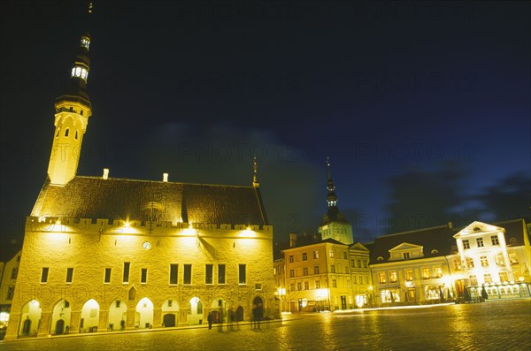 ESTONIA, Tallinn, Raekoja Plats.  Exterior of the town hall and nearby shops and restaurant illuminated at night.