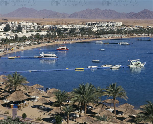 EGYPT, Red Sea Coast, Sharm el-Sheikh, "Naama Bay.  View over bay with jettys leading to tourist boats, encicled by sandy beach with thatched sun umbrellas and white sun loungers.  White painted buildings behind  "