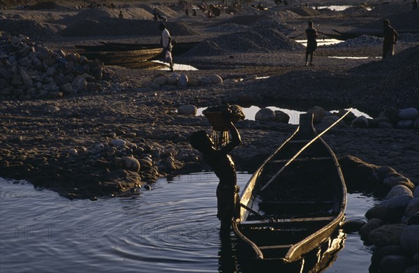 20017858 BANGLADESH  Jafflong Workers in stone quarry near water with man in foreground lifting basket of stones from wooden rowing boat.