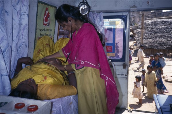INDIA, Karnataka, Bangalore, Female health worker examining a pregnant woman in a mobile clinic.  Children and woman seen outside through open door.