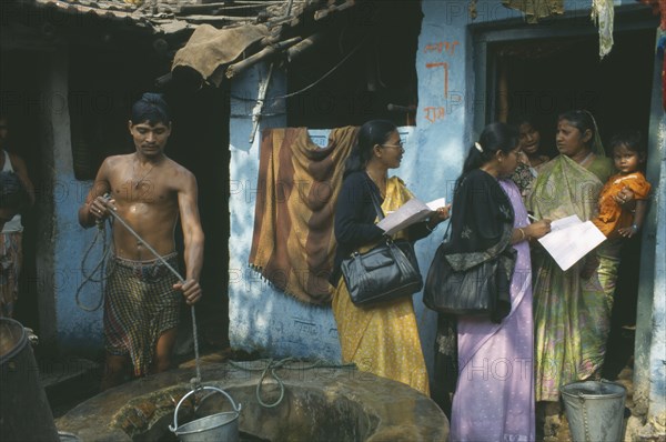 INDIA, Tamil Nadu, Madras, Women conducting a survey on reproductive health talk to a woman holding a child standing in the doorway of a house.  Man collecting water from well in the foreground.