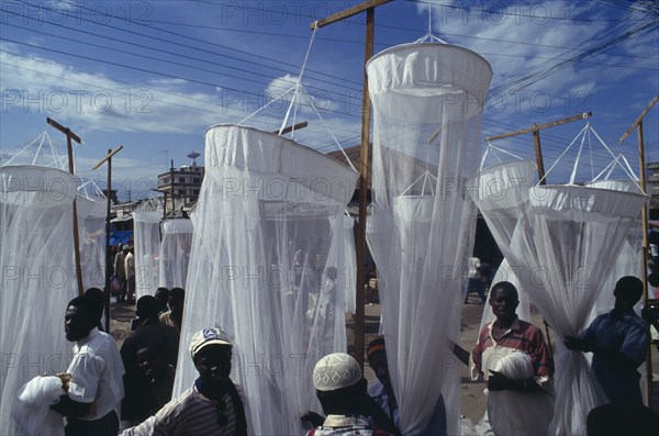 TANZANIA, Dar es Salaam, Mosquito nets for sale at market with men in the foreground and seen through the nets.