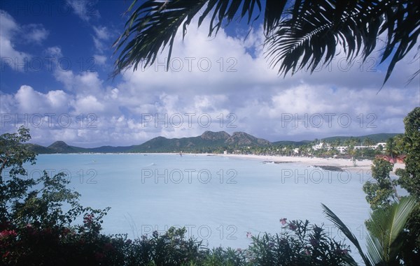 WEST INDIES, Antigua, Jolly Beach, View over water towards distant beach and coastline framed by overhanging palm fronds and other vegetation.