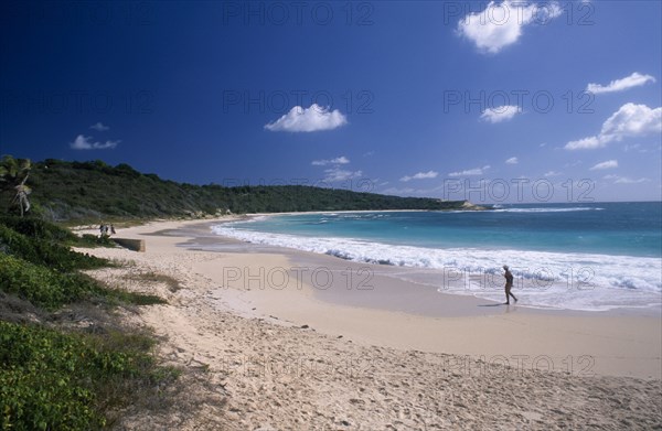 WEST INDIES, Antigua, Half Moon Bay, View over sandy beach and semicircular bay with woman walking along the waters edge.