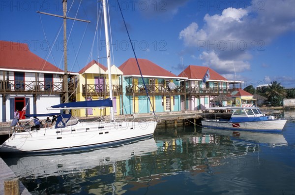 WEST INDIES, Antigua, St Johns, Redcliffe Quay.  Boats moored beside wooden jetty with colourful houses with red roof tops and painted window shutters behind.