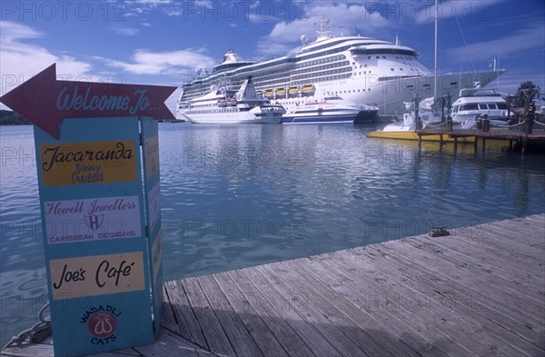 WEST INDIES, Antigua, St Johns, St Johns Harbour.  Wooden jetty in the foreground with painted sign directing visitors to shops and cafes.  Cruise boats in the water behind.