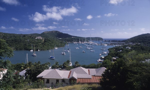 WEST INDIES, Antigua, Ordnance Bay, View over house rooftops towards bay with moored yachts and surrounding coastline.