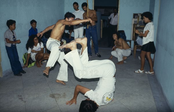 20018911 BRAZIL  Capoeira Local men in animated poses of martial arts  inside a small room with spectators.