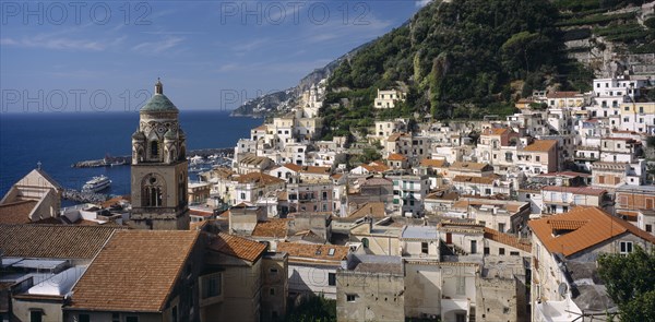 ITALY, Campania, Amalfi , View over red tiled roof tops of the town with the Duomo bell tower on the left and tree covered hillside behind.