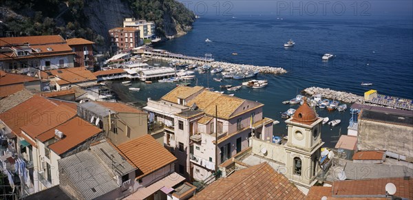 ITALY, Campania, Amalfi Coast, Sorrento.  View over red tiled roof tops and church bell tower towards Marina Grande and moored boats.