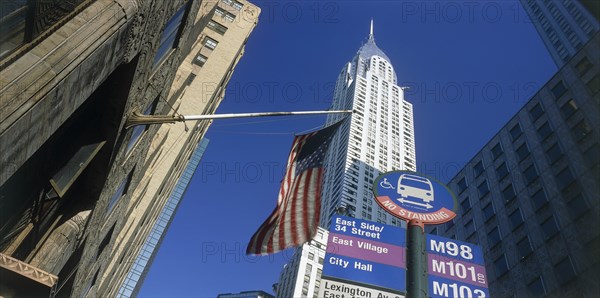 USA, New York State, New York, "Chrysler Building.  Seen from below, between other buildings with American Stars and Stripes flag and road sign in the foreground."