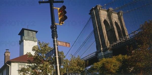 USA, New York State, New York, Part view of Brooklyn Bridge seen above trees with road sign and traffic lights in the foreground.
