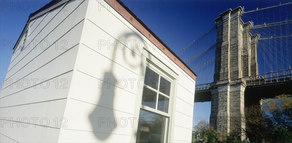 USA, New York , Manhattan, Part view of Brooklyn Bridge with shadow cast by street lamp on exterior wall of white painted building in the foreground.