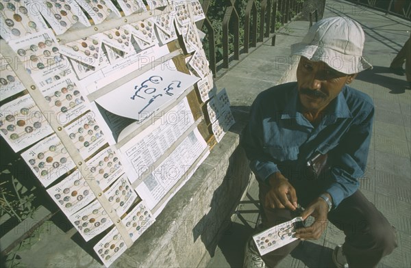 SYRIA, Damascus, Local street vendor selling lottery tickets on the side of a path.