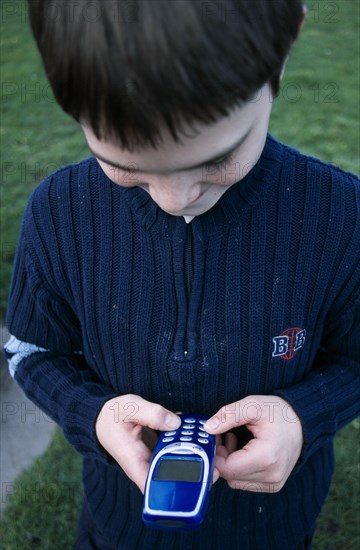 COMMUNICATIONS, Telephones, Mobile, Close up of a boy holding a blue mobile phone with thumbs on the dialing pad.