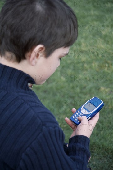 COMMUNICATIONS, Telephones, Mobile, View over the shoulder of a boy holding a blue mobile phone with his thumb on the dialing pad.