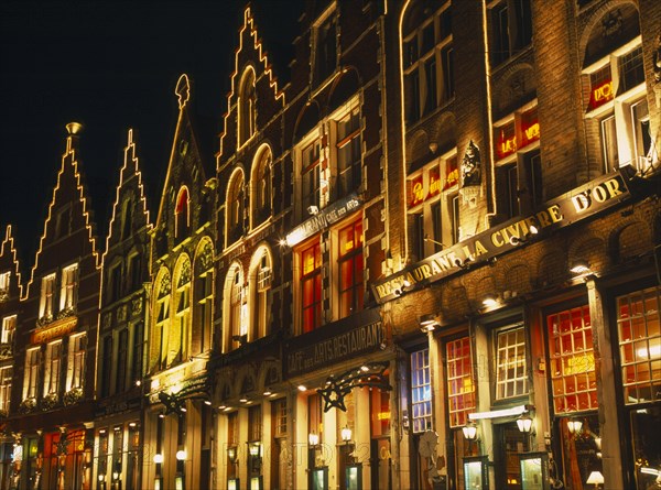 BELGIUM, West Flanders, Bruges, Grand Market. Shops and restaurant facades illuminated at night.