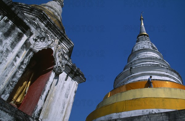 THAILAND, North, Chiang Mai, Wat Chedi Luang. Statue of standing Buddha in an alcove  beside a stuppa with a man walking around it