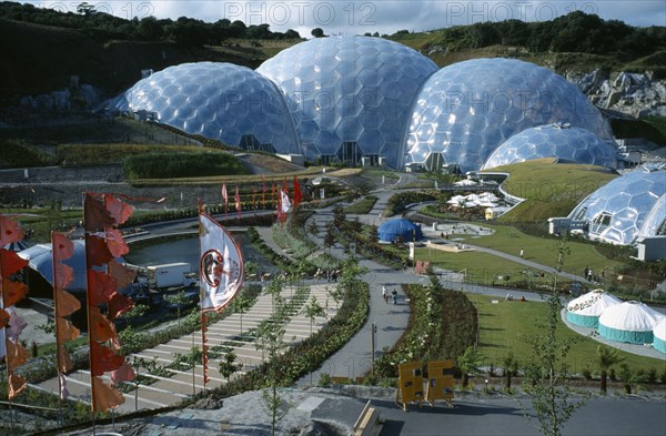 ENGLAND, Cornwall, St. Austell, Eden Project.  General view over the Humid tropics Biome exterior with line of coloured flags and visitors on path to entrance.