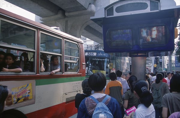 THAILAND, Bangkok, Bus and passengers at bus stop in Siam Square beside one video screen showing bus times and another a music video