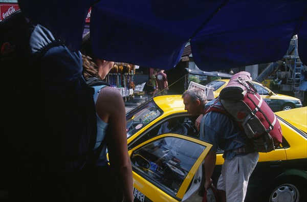 THAILAND, Bangkok, Khao San Road male backpacker talking to a taxi driver through the open passenger door whilst a  female backpacker looks on