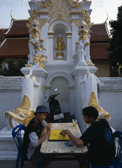 THAILAND, North, Chiang Mai, Wat Mahawan temple with two boys playing go on the pavement below temple wall carvings