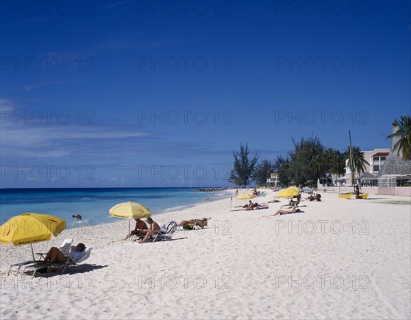 BARBADOS, South Coast, Dover Beach. , "Golden sandy beach lined with palms, with scattered bathers, sunbeds and umberellas and buildings partially hidden by trees."